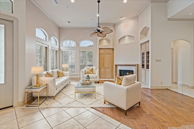 tiled living room featuring a high ceiling, a fireplace, ceiling fan, and crown molding