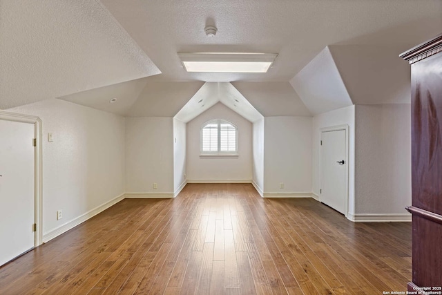 additional living space with lofted ceiling, a textured ceiling, and hardwood / wood-style floors