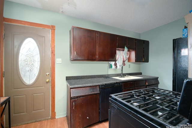 kitchen featuring gas range oven, dishwasher, sink, black refrigerator, and dark brown cabinetry