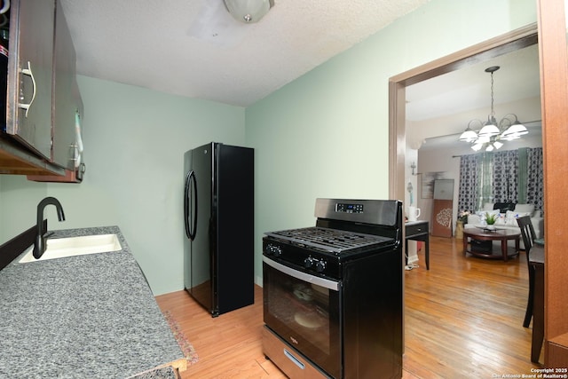 kitchen featuring black refrigerator, light wood-type flooring, stainless steel range with gas cooktop, sink, and an inviting chandelier