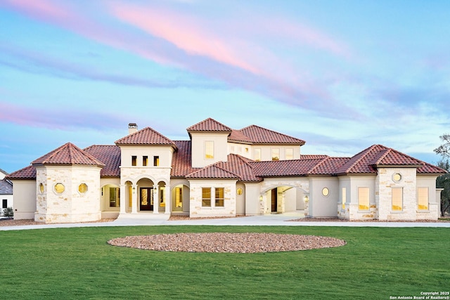 back house at dusk featuring a lawn