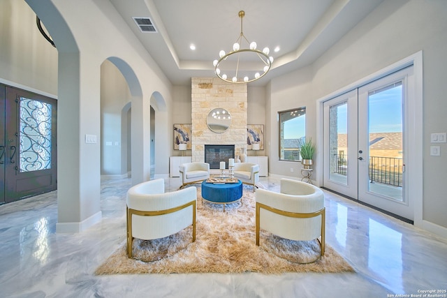 living room featuring a raised ceiling, a chandelier, french doors, a fireplace, and a high ceiling