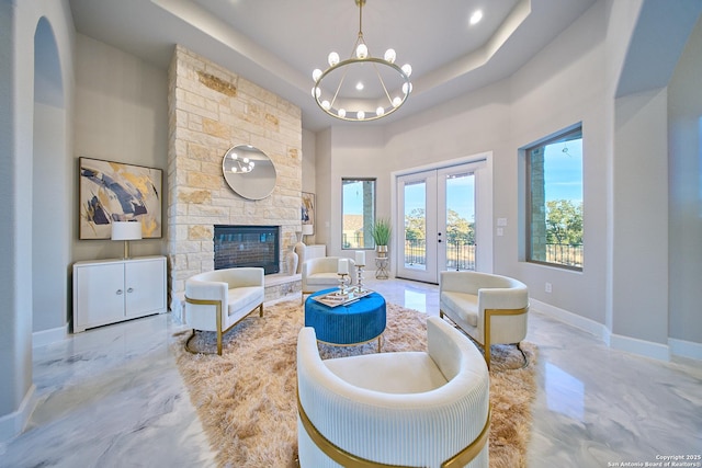 living room with french doors, a tray ceiling, and a stone fireplace