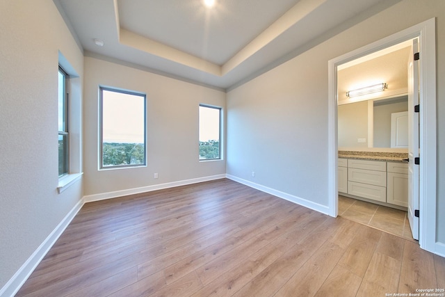 unfurnished bedroom featuring light hardwood / wood-style floors, ensuite bath, and a tray ceiling