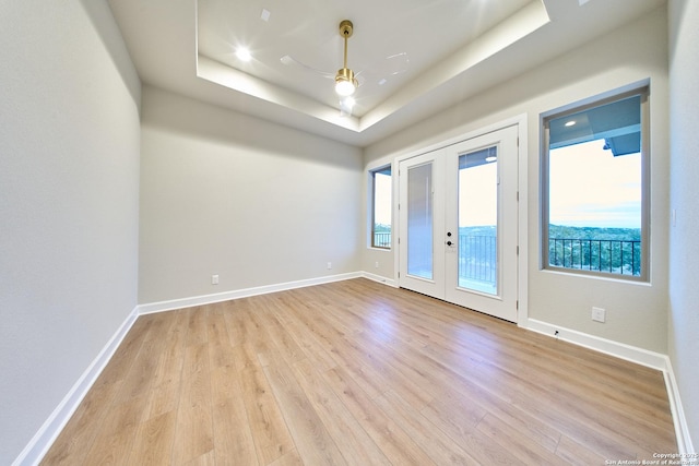 unfurnished room featuring ceiling fan, light wood-type flooring, french doors, and a tray ceiling