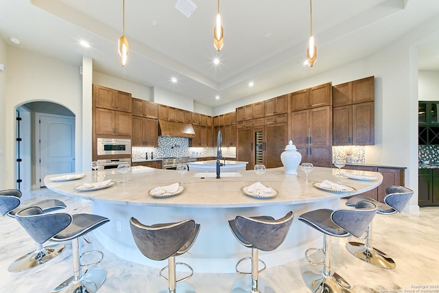 kitchen with stainless steel appliances, a large island with sink, custom range hood, sink, and decorative light fixtures