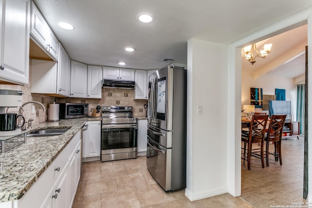 kitchen featuring appliances with stainless steel finishes, light stone counters, white cabinets, an inviting chandelier, and sink