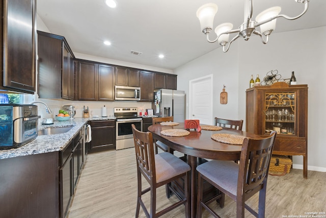 kitchen featuring appliances with stainless steel finishes, light hardwood / wood-style floors, pendant lighting, light stone counters, and sink