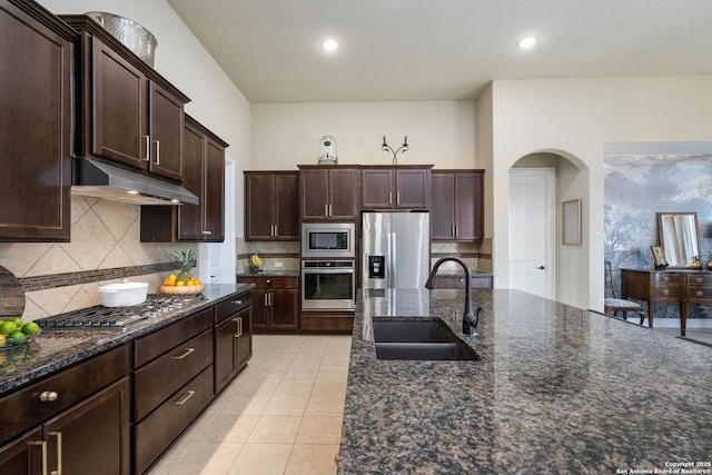 kitchen featuring sink, tasteful backsplash, dark brown cabinets, dark stone counters, and appliances with stainless steel finishes