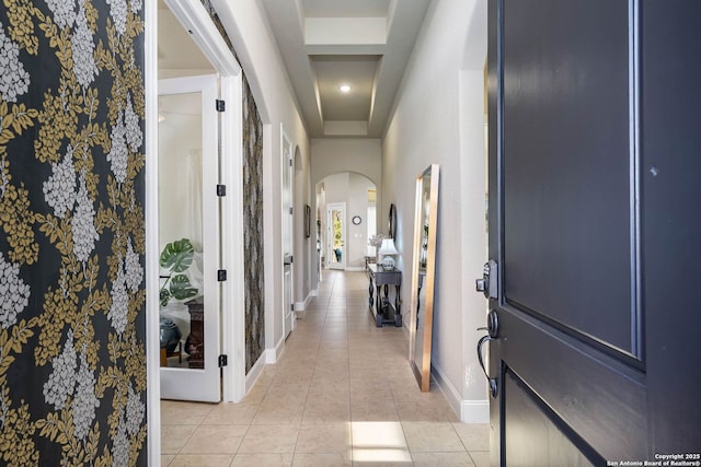 hallway featuring a tray ceiling and light tile patterned floors