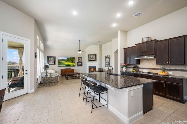 kitchen with sink, dark stone countertops, ceiling fan, an island with sink, and a breakfast bar