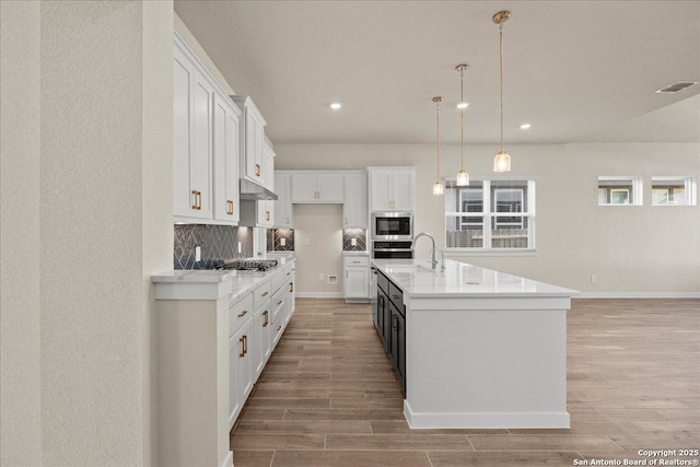 kitchen with a center island with sink, white cabinets, tasteful backsplash, and appliances with stainless steel finishes