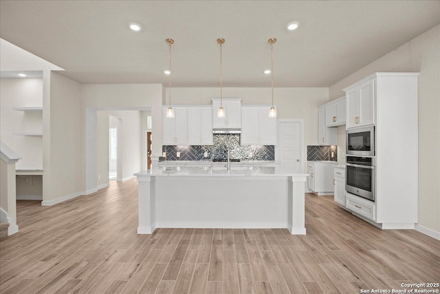 kitchen featuring a center island with sink, built in microwave, stainless steel oven, and white cabinetry