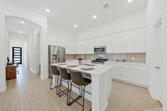 kitchen featuring a center island with sink, white cabinetry, a breakfast bar, and appliances with stainless steel finishes