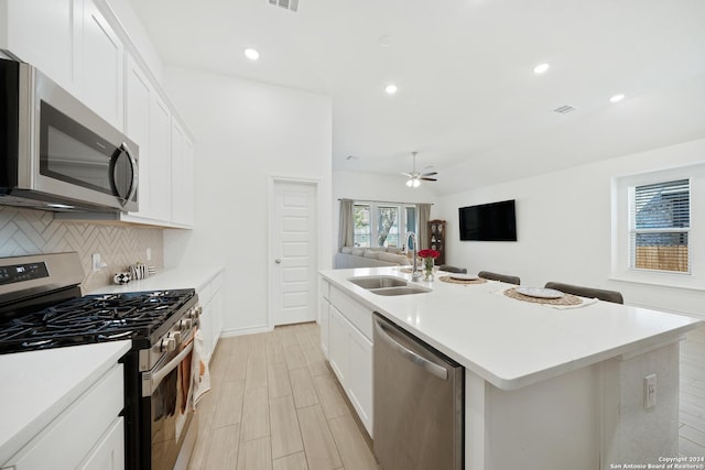 kitchen with white cabinets, stainless steel appliances, an island with sink, ceiling fan, and sink