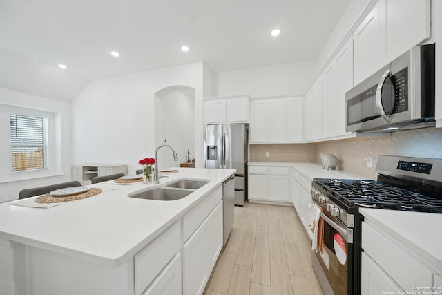 kitchen with vaulted ceiling, a kitchen island with sink, white cabinets, appliances with stainless steel finishes, and sink