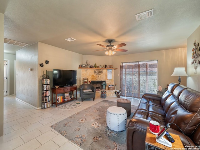 living room with a textured ceiling, ceiling fan, light tile patterned floors, and a stone fireplace