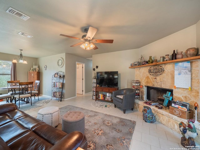 tiled living room featuring a stone fireplace and ceiling fan with notable chandelier