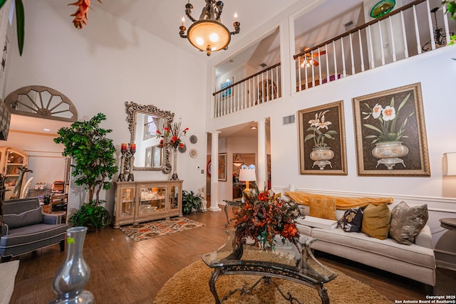 living room featuring hardwood / wood-style floors, decorative columns, a chandelier, and a high ceiling