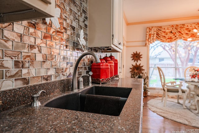 kitchen featuring sink, white cabinets, decorative backsplash, dark stone counters, and crown molding