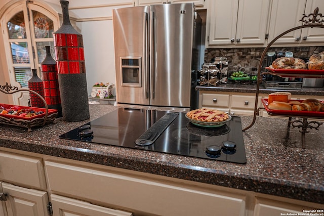 kitchen with backsplash, hanging light fixtures, stainless steel refrigerator with ice dispenser, black electric cooktop, and dark stone counters