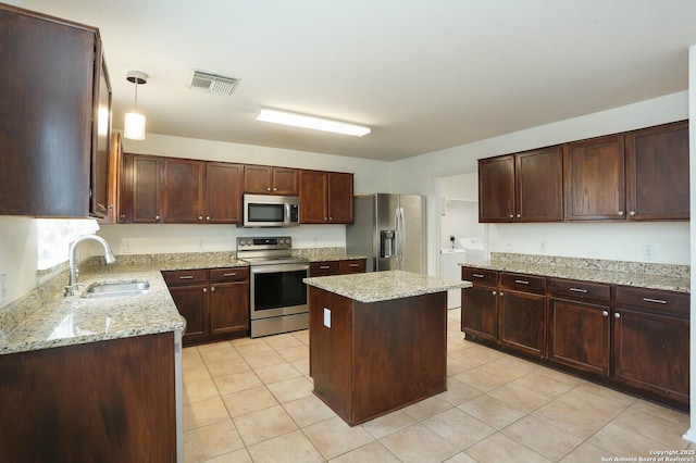 kitchen featuring a center island, decorative light fixtures, appliances with stainless steel finishes, washing machine and clothes dryer, and sink