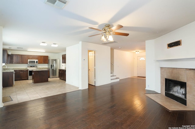 unfurnished living room with light hardwood / wood-style floors, ceiling fan, a tile fireplace, and sink