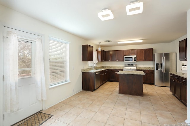 kitchen with stainless steel appliances, sink, a center island, light tile patterned flooring, and dark brown cabinets