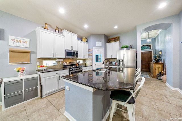 kitchen with an island with sink, decorative backsplash, white cabinets, appliances with stainless steel finishes, and sink