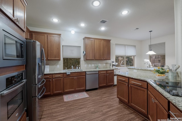 kitchen with dark wood-type flooring, tasteful backsplash, decorative light fixtures, appliances with stainless steel finishes, and light stone countertops