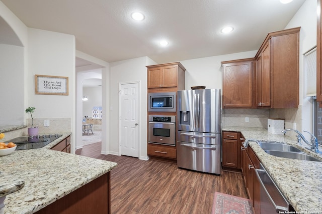 kitchen with tasteful backsplash, sink, stainless steel appliances, light stone countertops, and dark wood-type flooring