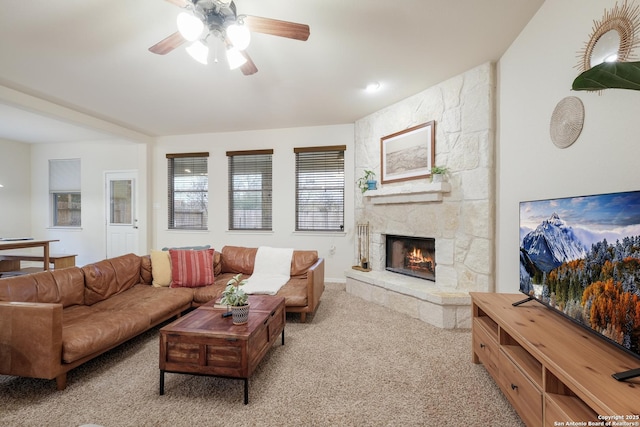 carpeted living room with ceiling fan and a stone fireplace