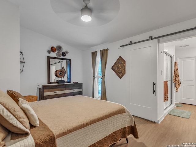 bedroom with ceiling fan, light hardwood / wood-style flooring, and a barn door