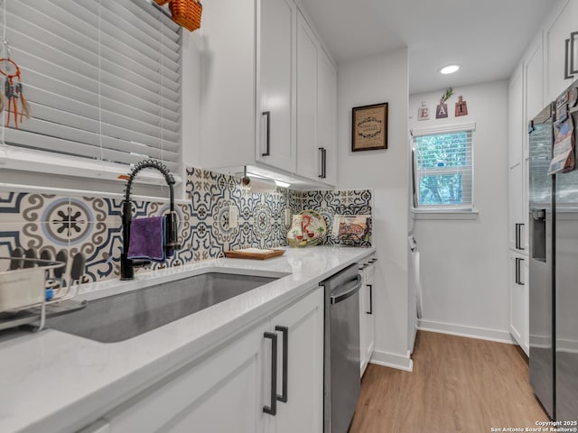 kitchen featuring white cabinets, stainless steel appliances, decorative backsplash, sink, and light wood-type flooring