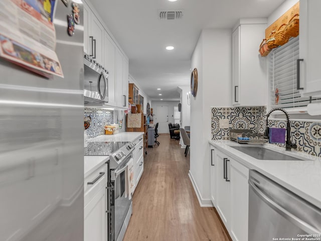 kitchen featuring tasteful backsplash, sink, white cabinetry, light wood-type flooring, and appliances with stainless steel finishes