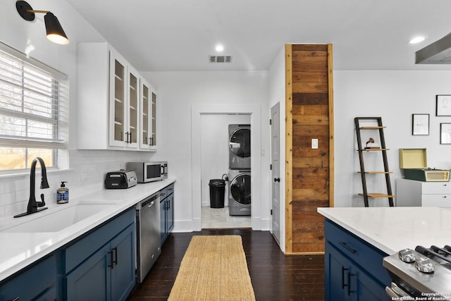 kitchen with sink, stacked washing maching and dryer, white cabinetry, blue cabinetry, and appliances with stainless steel finishes