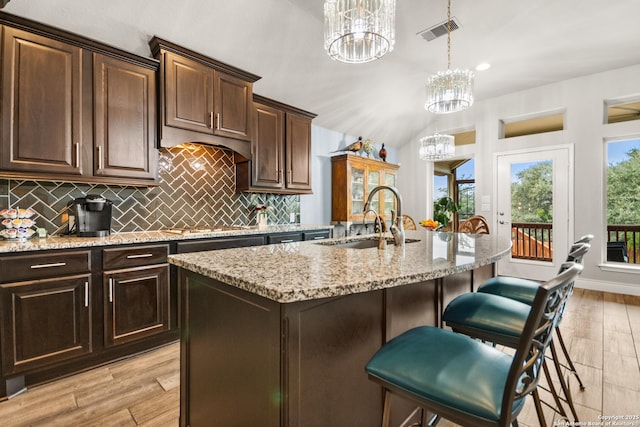 kitchen featuring sink, decorative light fixtures, light hardwood / wood-style floors, a kitchen island with sink, and a notable chandelier