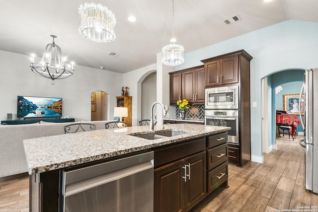 kitchen with a chandelier, appliances with stainless steel finishes, an island with sink, sink, and dark brown cabinets