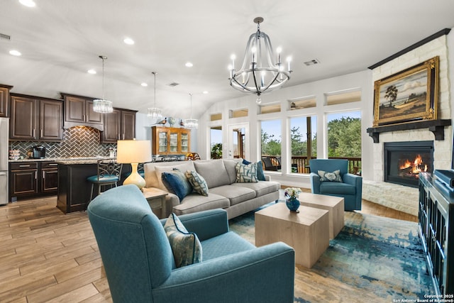 living room featuring an inviting chandelier, light hardwood / wood-style floors, and a stone fireplace