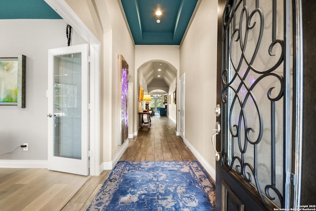 hallway featuring french doors, a raised ceiling, and wood-type flooring