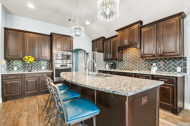 kitchen featuring a center island with sink, appliances with stainless steel finishes, hanging light fixtures, dark brown cabinetry, and sink