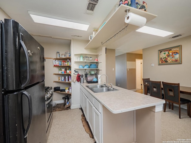 kitchen with black fridge, kitchen peninsula, white cabinetry, and sink