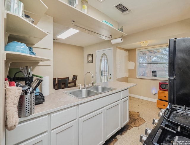 kitchen with black fridge, white cabinets, range with gas stovetop, and sink