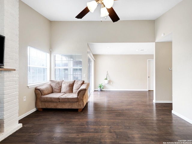 living room featuring ceiling fan, dark wood-type flooring, a brick fireplace, and a wealth of natural light