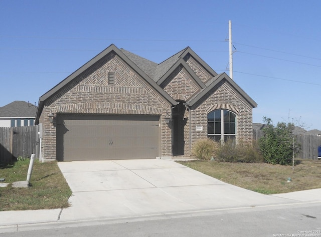 french country inspired facade with a garage, concrete driveway, roof with shingles, fence, and brick siding