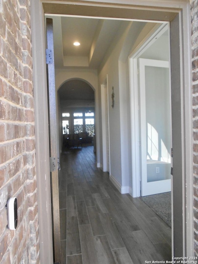 hallway featuring arched walkways, baseboards, a raised ceiling, and wood tiled floor