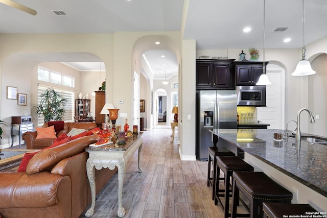 kitchen with a breakfast bar area, appliances with stainless steel finishes, hanging light fixtures, dark stone counters, and sink