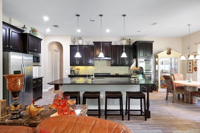 kitchen featuring appliances with stainless steel finishes, a kitchen breakfast bar, decorative backsplash, and a center island with sink