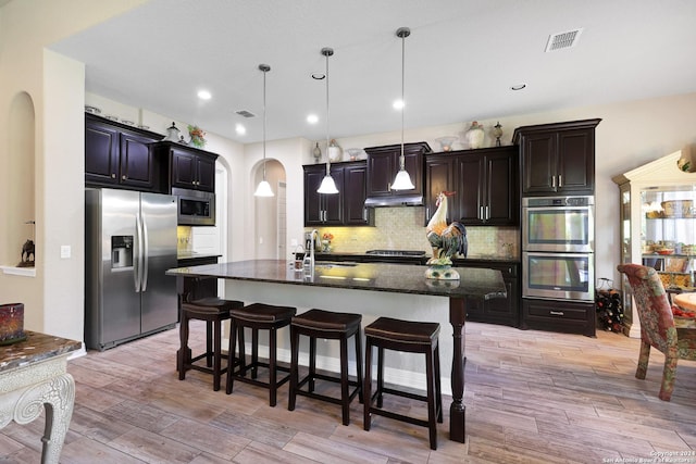 kitchen with appliances with stainless steel finishes, pendant lighting, a breakfast bar, and a kitchen island with sink