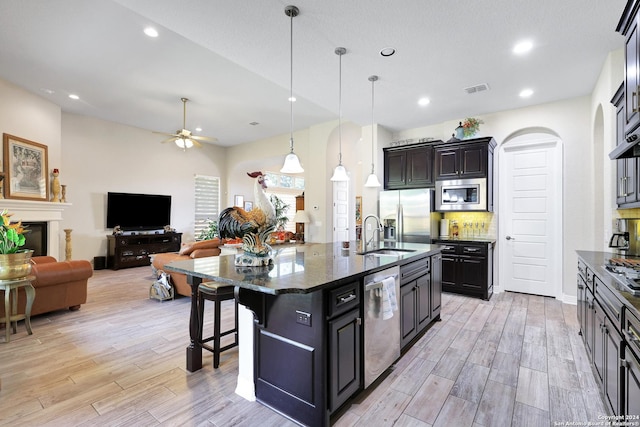 kitchen with appliances with stainless steel finishes, an island with sink, ceiling fan, pendant lighting, and a kitchen bar